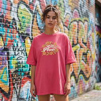 T-shirt femme oversized rose imprime Girl Power et fleurs retro, porte devant un mur de graffitis colores