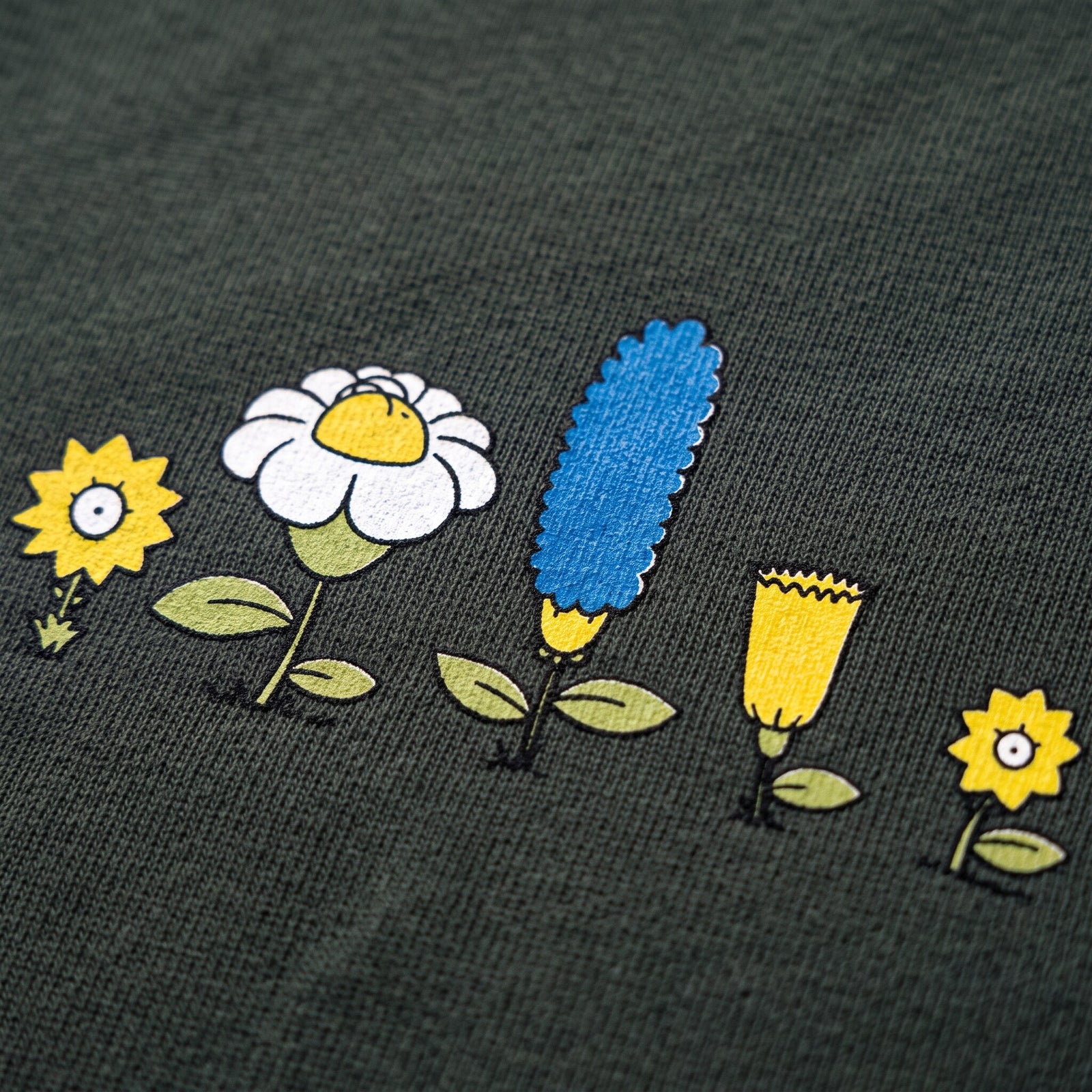 Gros plan sur les cinq fleurs cartoon jaunes, blanche et bleue imprimées sur le coton vert sapin du t-shirt