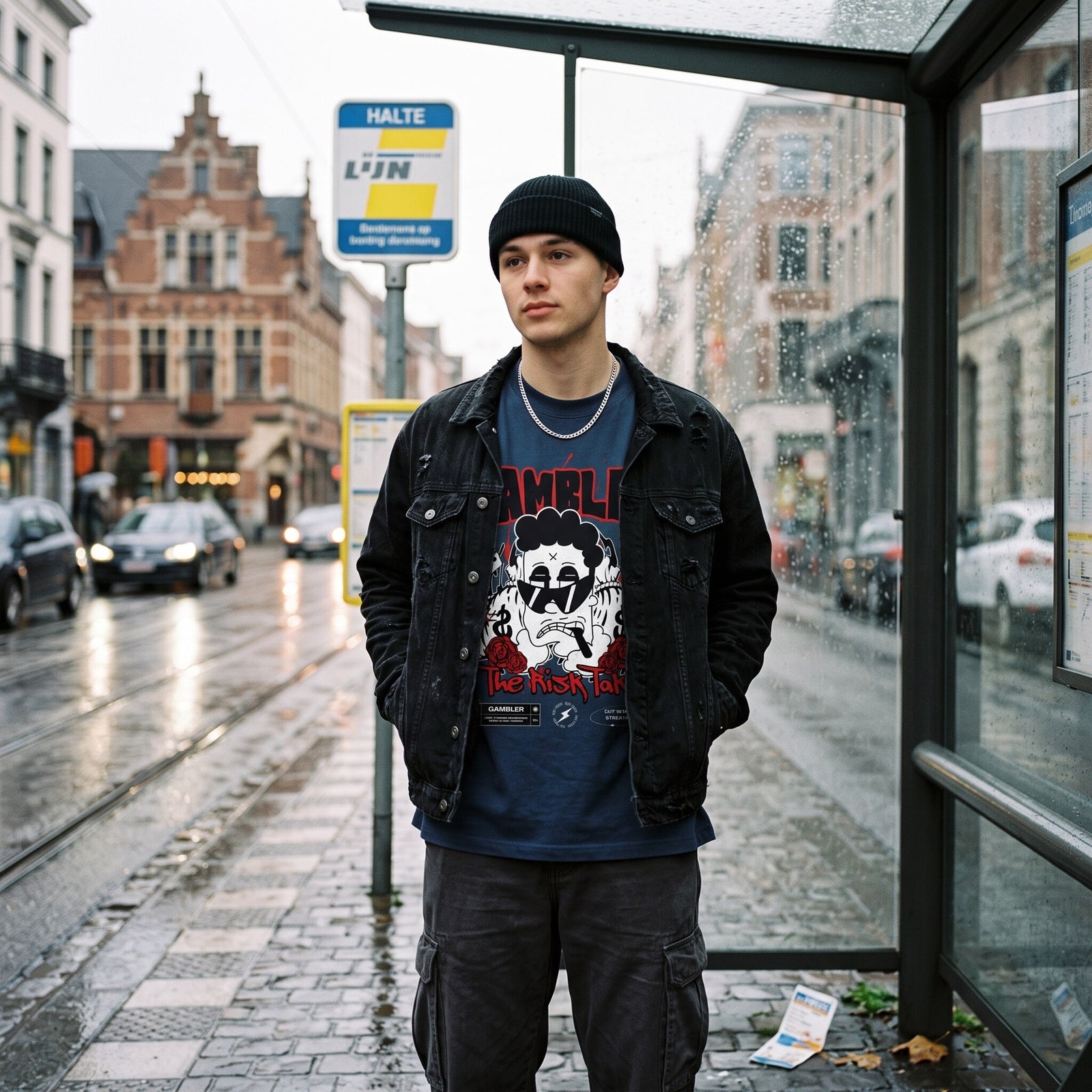 T-shirt bleu nuit Gambler porte sous une veste en jean noire, a un arret de tram belge sous la pluie