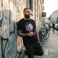 T-shirt geek noir porté par un homme en rue devant un mur graffé, look streetwear urbain