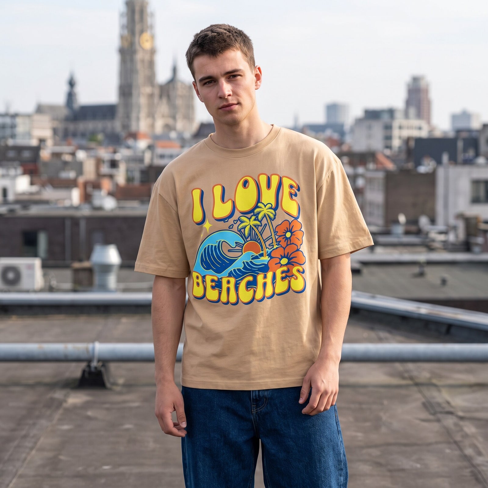 T-shirt sable I Love Beaches et jean large, portes sur un toit gravillonne dominant les toits de la ville
