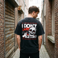 Dos d'un t-shirt noir délavé I Don't Care Anymore, crâne aux yeux rouges, dans une ruelle aux rideaux métalliques