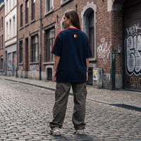 Femme streetwear portant le t-shirt Le Pays de la Bière bleu marine dans une rue belge - vue de dos drapeau belge, format carré