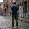 Homme streetwear portant le t-shirt Le Pays de la Bière bleu marine dans une rue belge - vue de dos drapeau belge, format carré