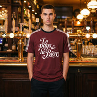 T-shirt bordeaux à bandes blanches Le pays de la Bière porté devant les pompes en laiton d'un bar belge