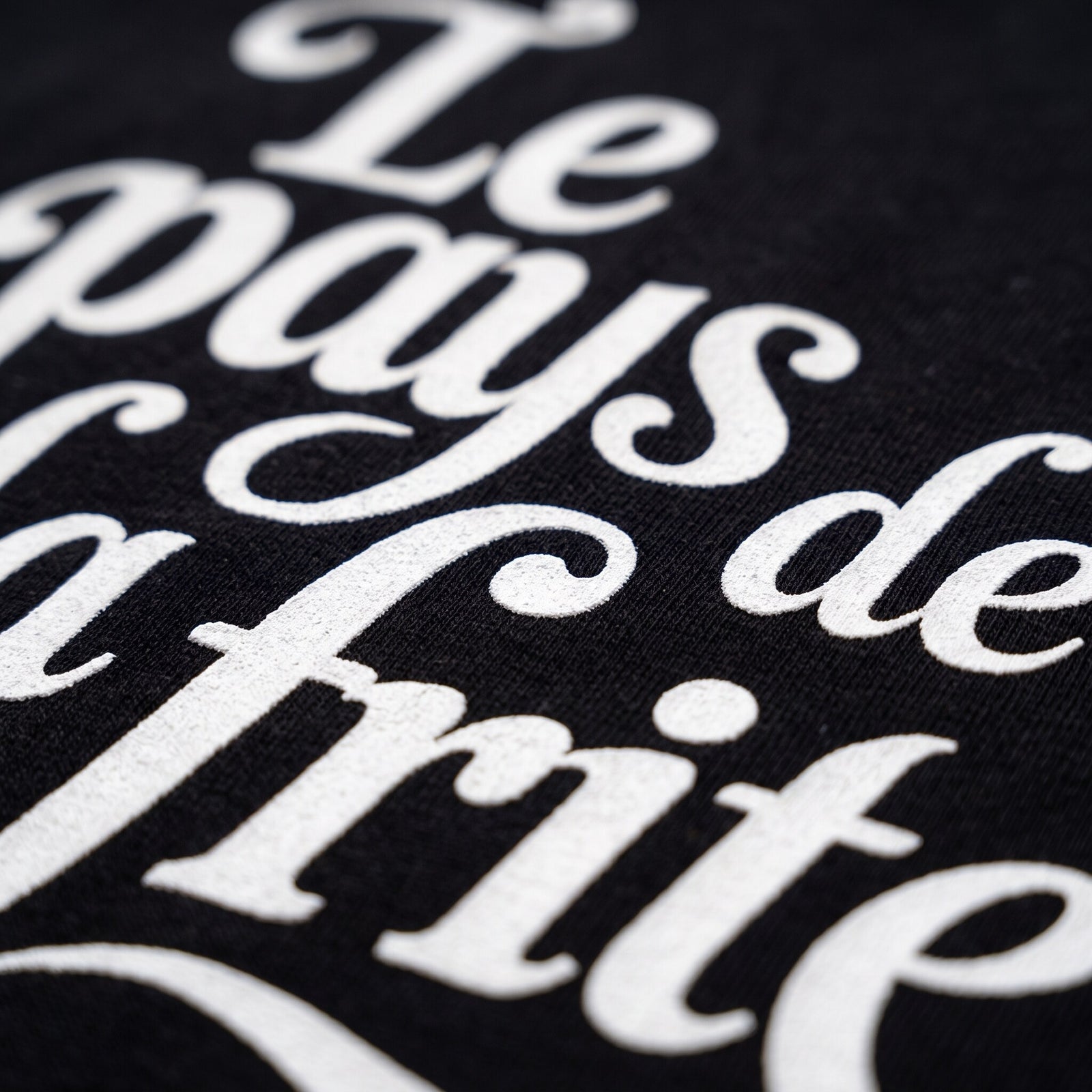 Gros plan sur la typographie cursive crème Le pays de la frite imprimée sur le coton noir du t-shirt