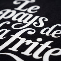 Gros plan sur la typographie cursive crème Le pays de la frite imprimée sur le coton noir du t-shirt
