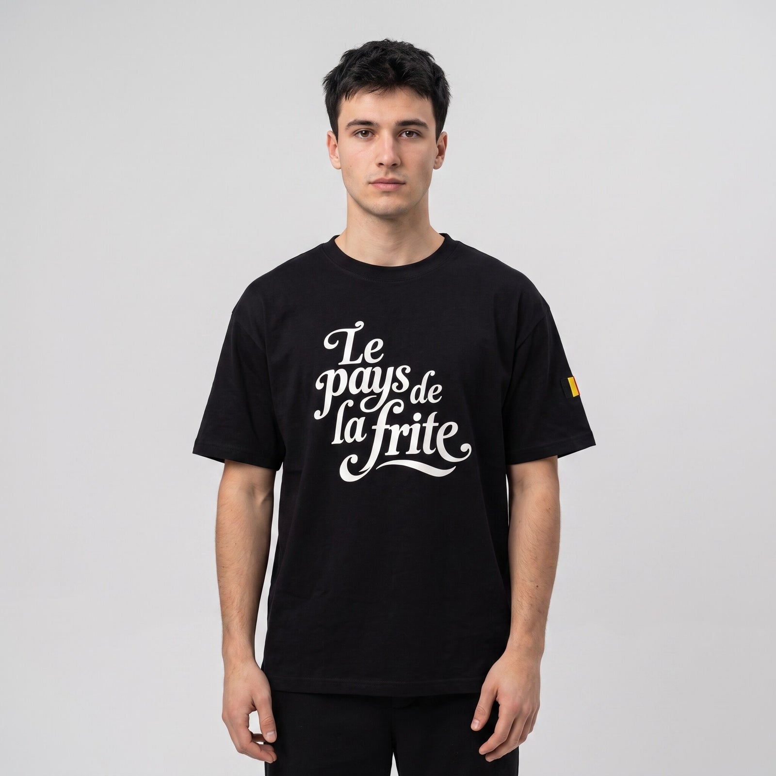 T-shirt oversized noir au lettrage cursif Le pays de la frite, porté en studio sur fond gris clair