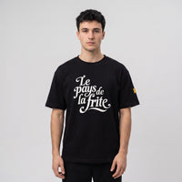T-shirt oversized noir au lettrage cursif Le pays de la frite, porté en studio sur fond gris clair