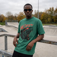 T-shirt Valiancy vert emeraude et lettrage rouge, porte dans un skatepark desert aux arbres d'automne