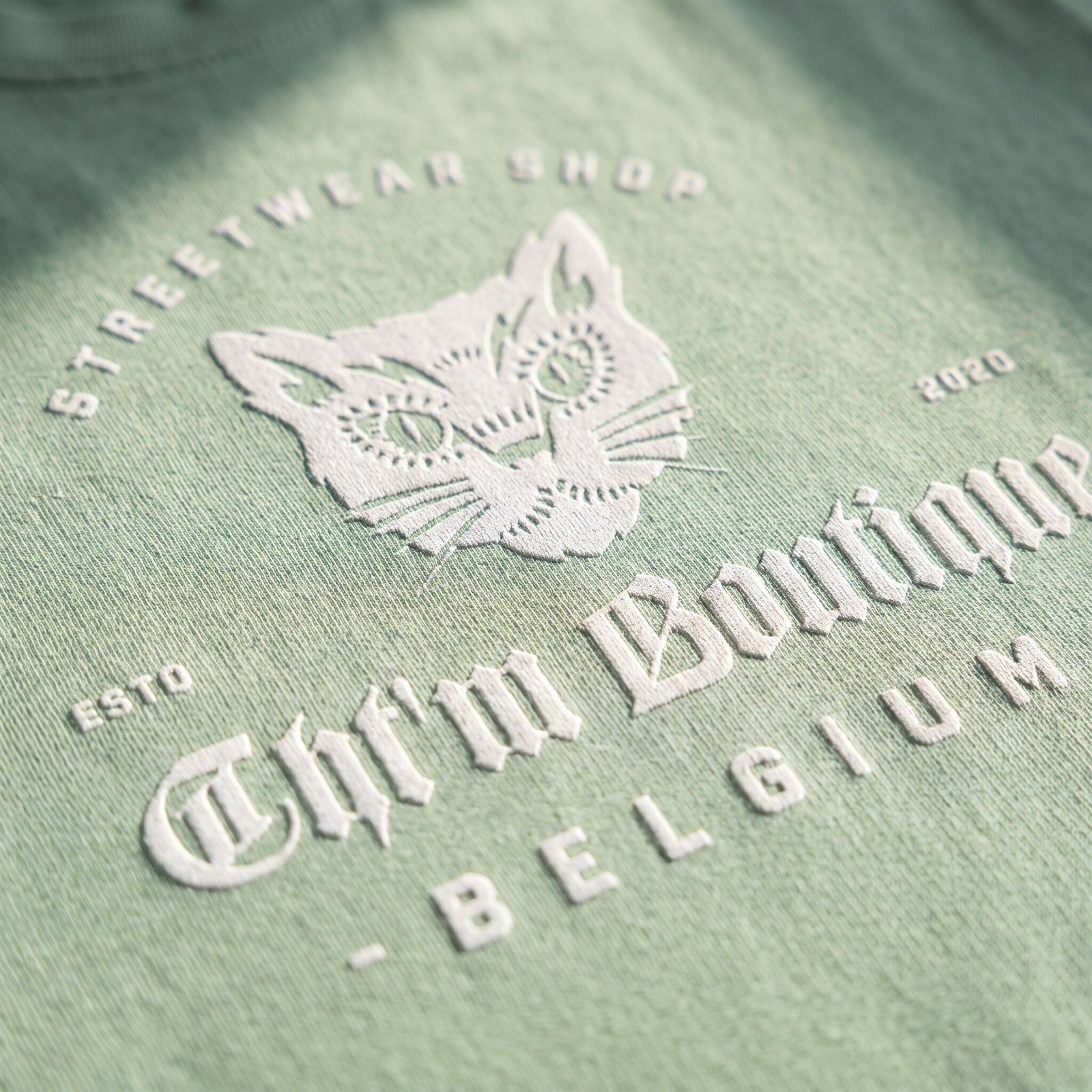 Gros plan sur l'impression blanche du chat gothique et du lettrage Belgium sur le coton vert amande