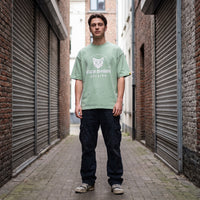 T-shirt oversized vert amande au logo chat gothique CHT'M Boutique Belgium, porté dans une ruelle pavée aux rideaux métalliques