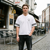 Maillot mesh blanc a col V et bandes noires, logo DAD a la chope, porte devant un cafe belge Duvel et Leffe