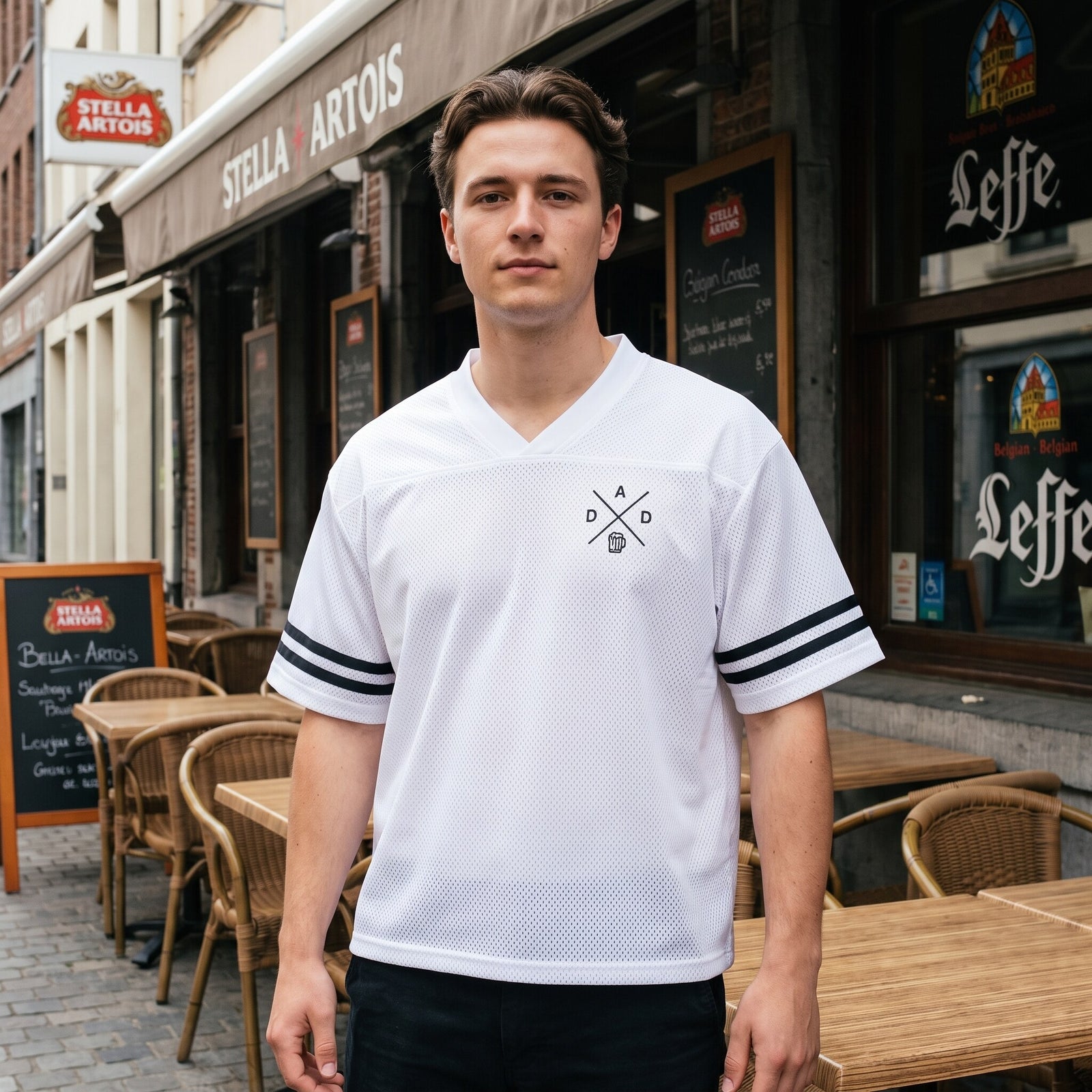Maillot de sport blanc en mesh, bandes noires aux manches, porte devant une terrasse en rotin d'un cafe belge