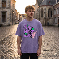 T-shirt oversized violet clair No More War, lettrage bulle et main en V, porté dans une ruelle pavée ancienne