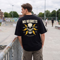 T-shirt noir oversized vu de dos, crâne No Regrets, devant un mur de graffitis et des skateurs en pleine session