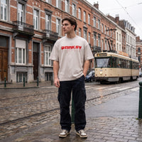 T-shirt oversized Banksy blanc cassé CHT'M porté avec un cargo noir, rue pavée mouillée et vieux tram crème