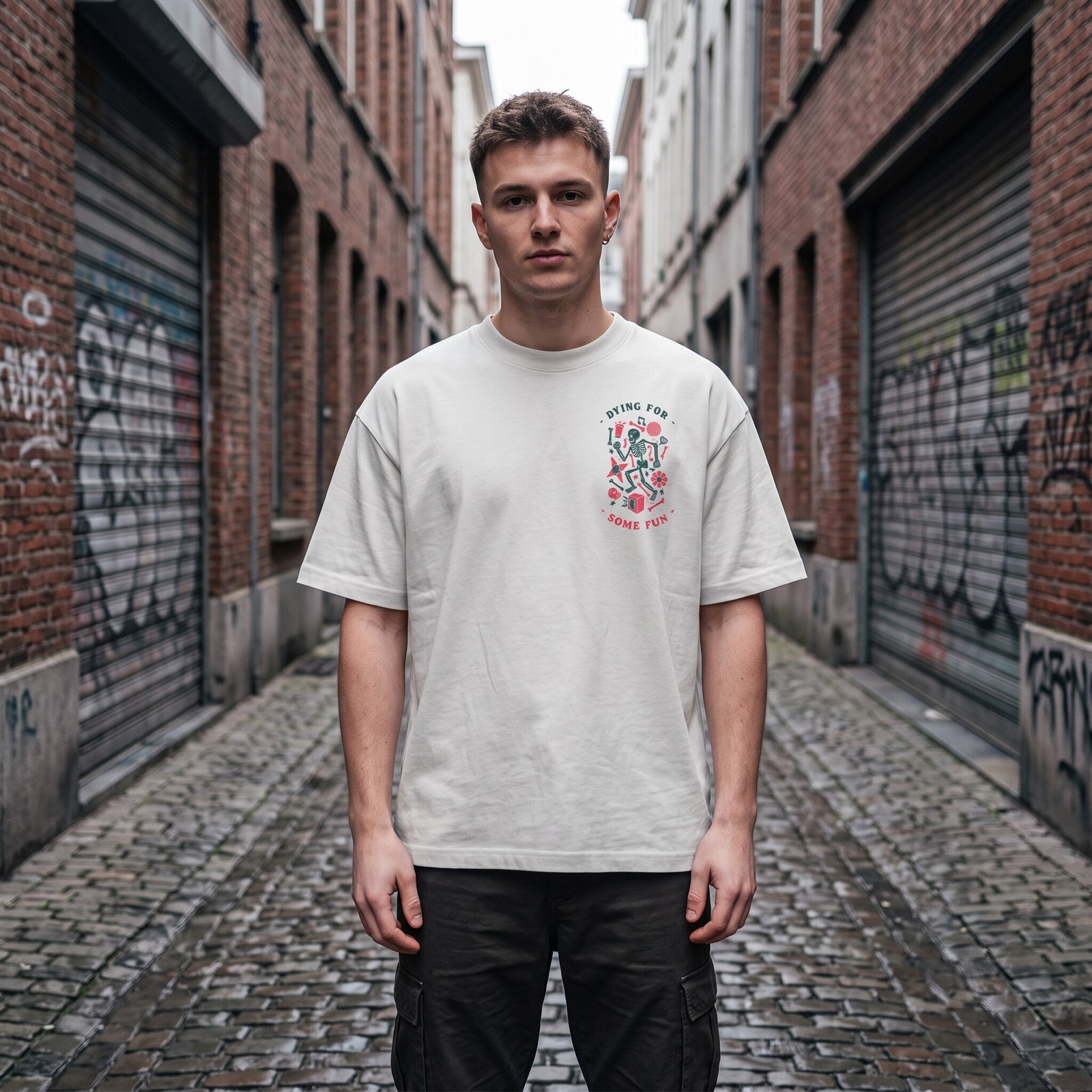 T-shirt oversized blanc casse Dying For Some Fun, porte dans une ruelle pavee bordee de rideaux metalliques tagues
