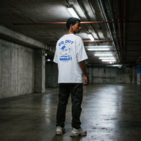 T-shirt blanc oversized porte de dos en pied avec un cargo noir, dans une allee de parking souterrain