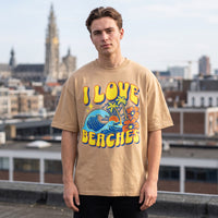 T-shirt oversized sable au lettrage jaune I Love Beaches, porte sur une toiture avec la ville en arriere-plan