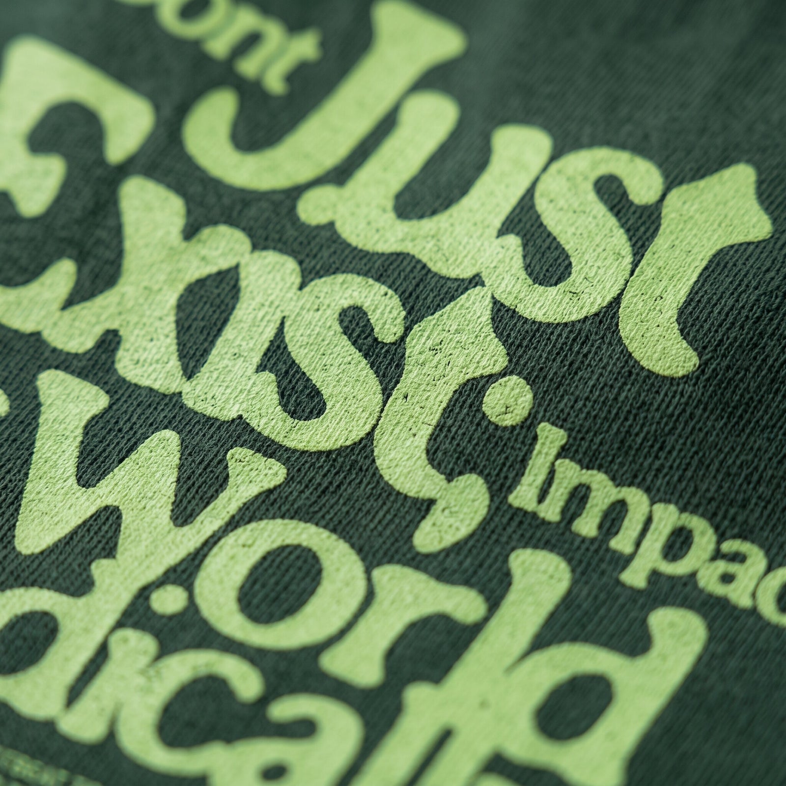 Gros plan sur le lettrage vert clair Don't Just Exist imprime sur le coton vert fonce d'un t-shirt en coton lourd