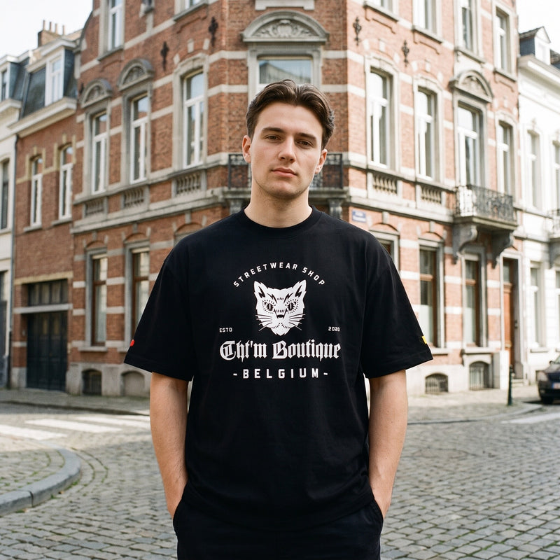 T-shirt oversized noir au logo chat blanc CHT'M Boutique Belgium, porte a un coin de rue pavee bruxelloise