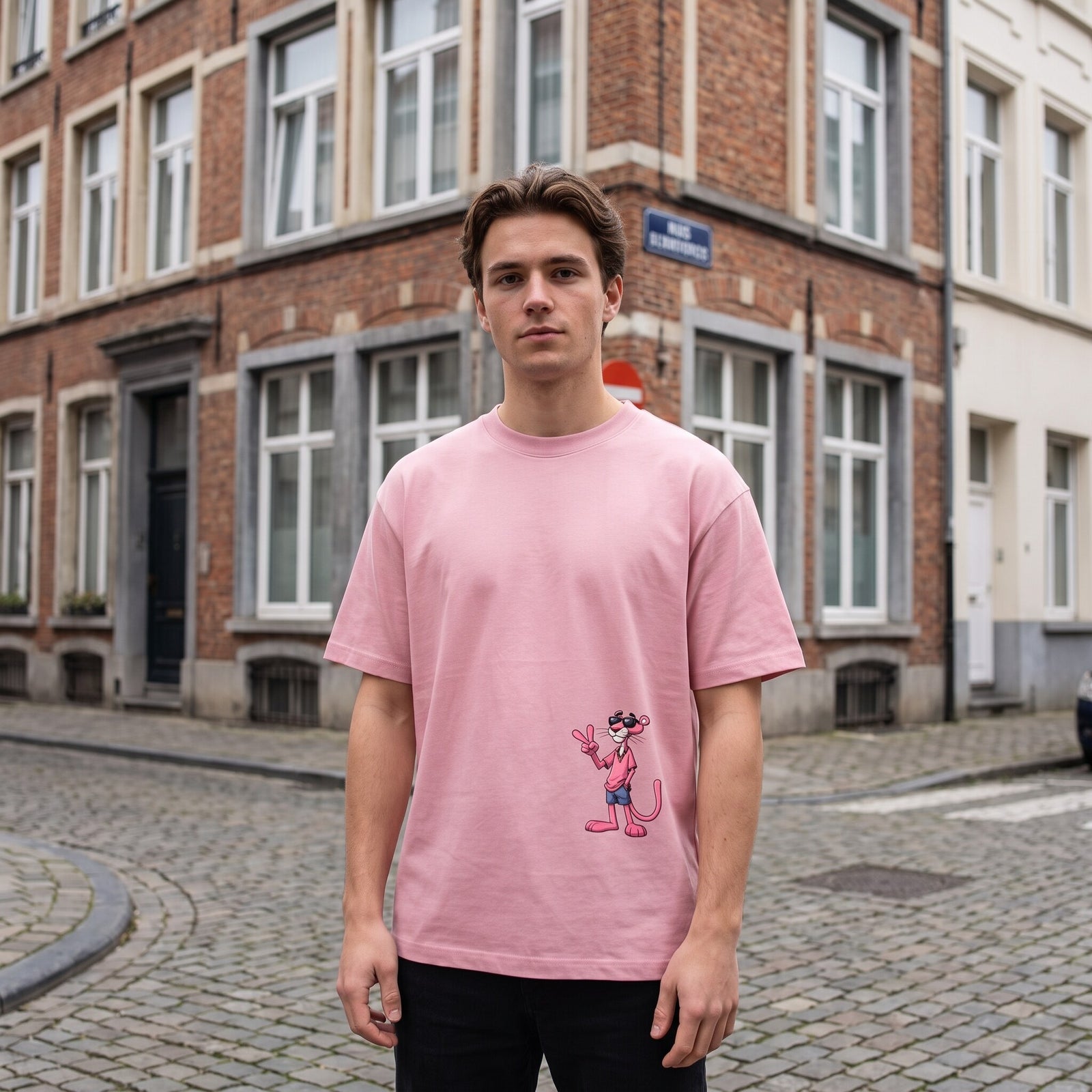 T-shirt rose coupe oversized, panthere rose a lunettes noires, porte a un coin de rue pavee en briques belges