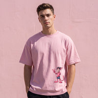 T-shirt rose oversized a la panthere cartoon faisant le signe V, porte devant un mur peint en rose pale