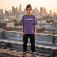 T-shirt oversized violet lettrage rose paradise, porte sur un toit face aux gratte-ciel au coucher du soleil