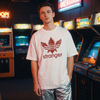 T-shirt oversized blanc au logo stranger rouge, porte dans une salle d'arcade retro aux neons colores