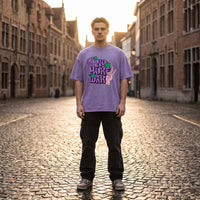 T-shirt violet clair aux fleurs vertes et symbole peace, porté à contre-jour dans une rue pavée au soleil couchant