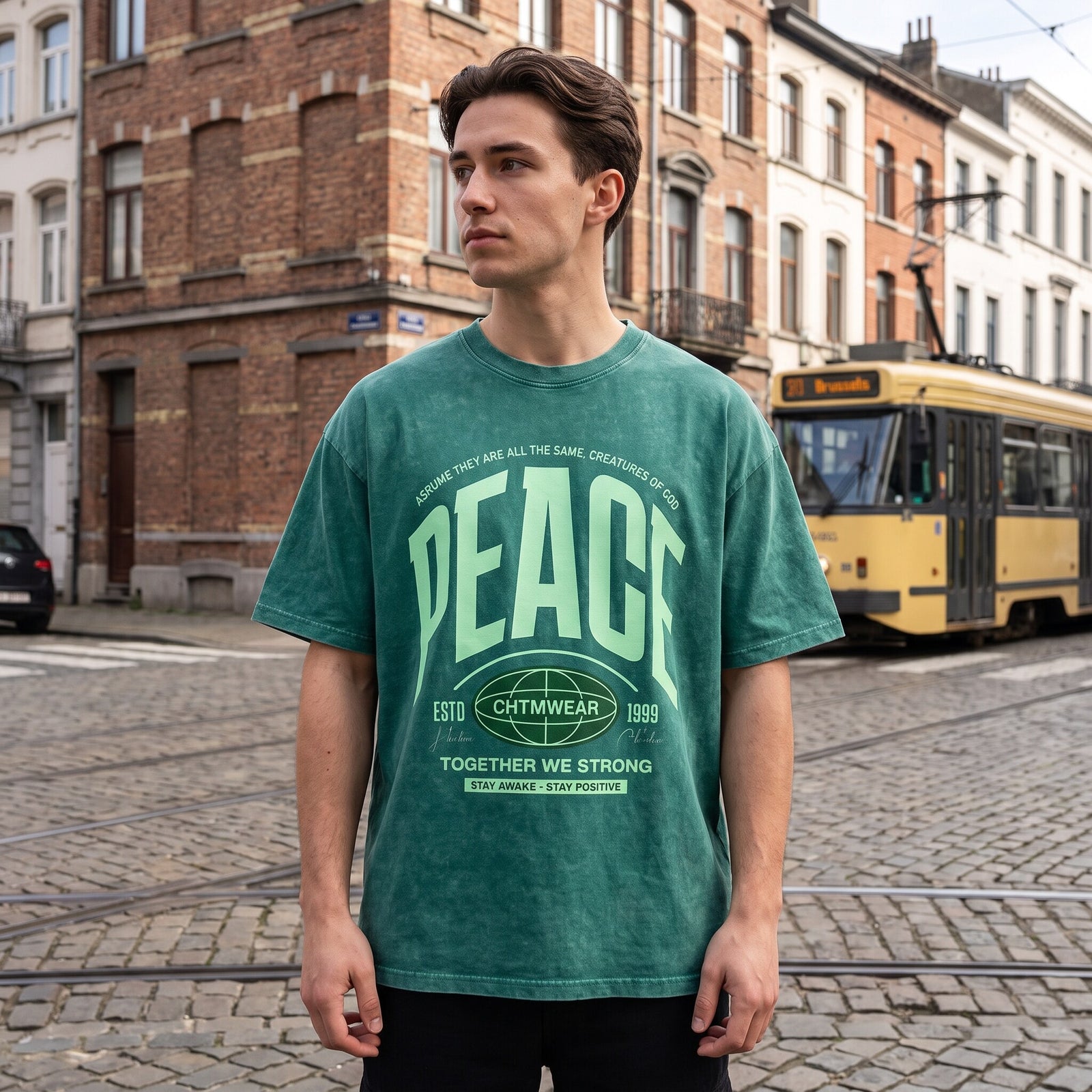 Coupe oversized du t-shirt PEACE vert, cadrage taille devant un vieux tram jaune et les rails a Bruxelles