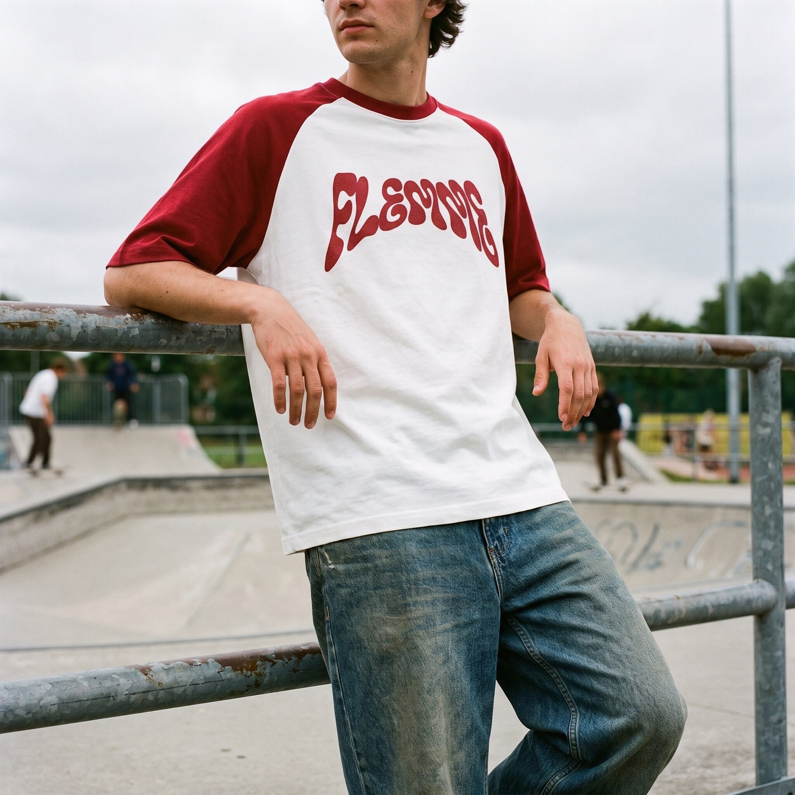 T-shirt raglan blanc, gros lettrage psychédélique bordeaux FLEMME, cadrage serré avec jean délavé au skatepark