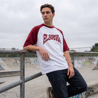 T-shirt oversized FLEMME à manches bordeaux, appuyé sur la rambarde d'un skatepark sous un ciel gris
