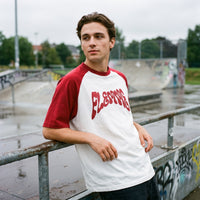 T-shirt raglan blanc et bordeaux FLEMME en typographie psychédélique, porté dans un skatepark détrempé