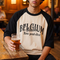 T-shirt raglan ecru et noir au lettrage varsity Belgium, porte attable dans un cafe brun devant un verre de biere