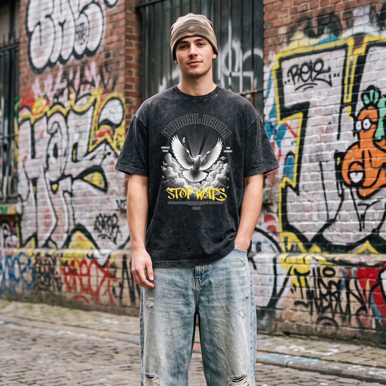 T-shirt noir délavé Stop Wars porté avec un bonnet beige et un jean clair déchiré devant une fresque de street art
