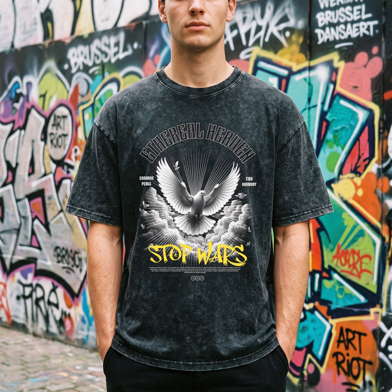 Gros plan sur un t-shirt noir délavé Stop Wars, colombe blanche et lettrage jaune, devant un mur de graffitis