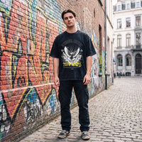 Silhouette oversized en t-shirt noir délavé Stop Wars, debout sur les pavés d'une ruelle bruxelloise peinte