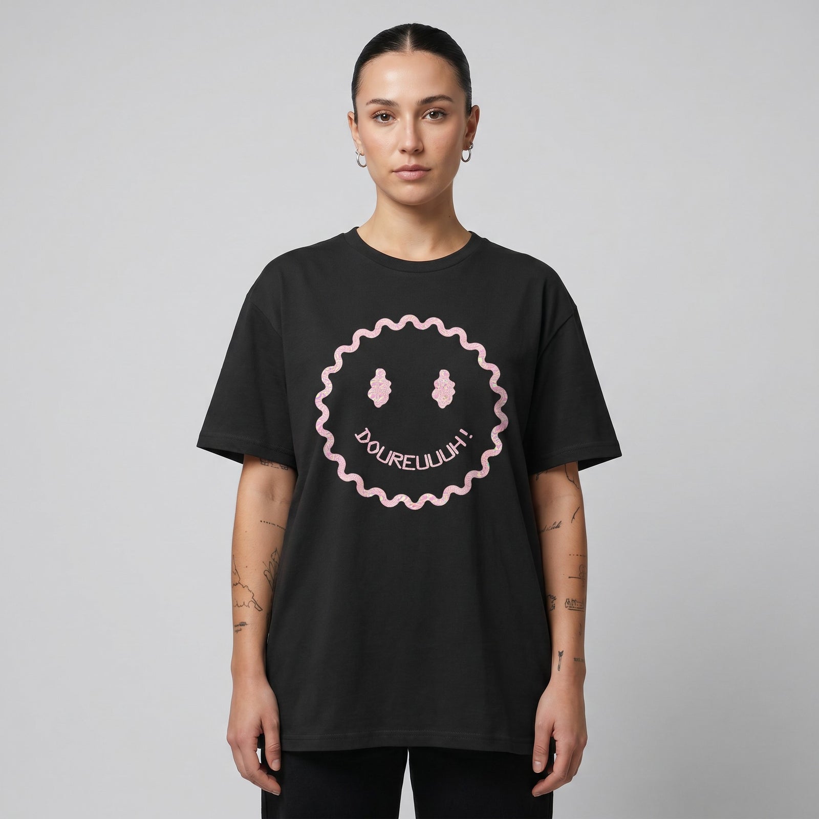 T-shirt Dour Festival DOUREUUUH oversize noir porté par une femme, smiley acid holographique, studio